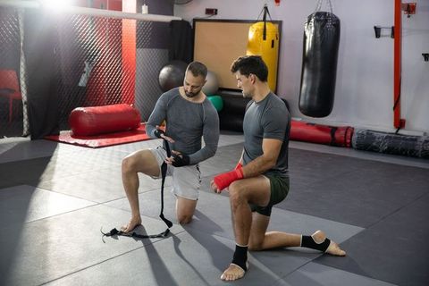 Kneeling mma partners wrapping hands before sparring in mixed martial arts gym