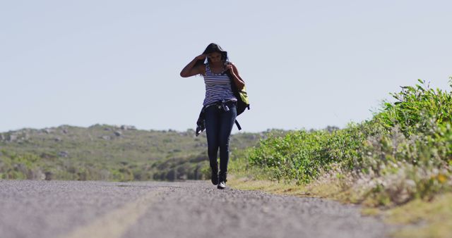 African american woman with backpack walking on a roadside highway. road trip travel and adventure concept
