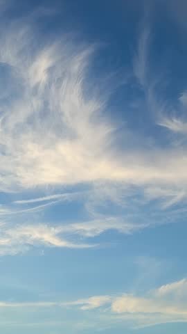 Vertical aerial video capturing wispy cirrus clouds drifting across golden evening sky