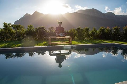 Sunlit poolside meditation with mountain reflection, asian man sitting cross-legged bench