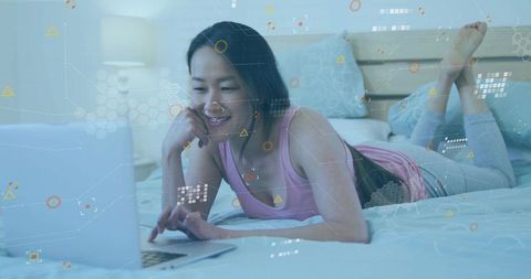 Korean woman relaxing on bed using laptop with holographic tech overlay for remote work