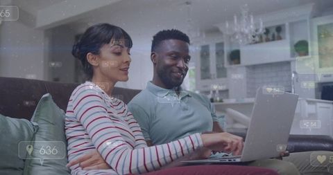 Diverse couple sharing laptop on sofa in modern open-plan living room, reacting to social ui