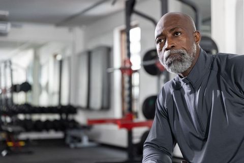 Mature african american man resting in gym, eyeing dumbbell rack with serious focus
