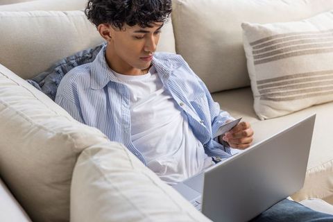 Young adult shopping online via laptop in cozy living room