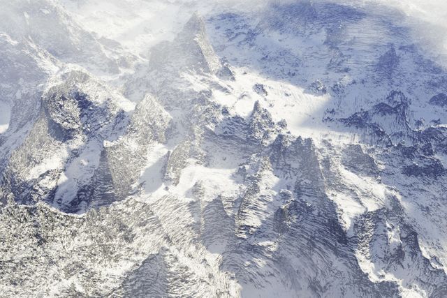 Stunning visual showing snow-covered mountain peaks from above in winter season. Suitable for travel magazines, outdoor adventure blogs, winter sports promotions, and wall art decorating nature enthusiasts' spaces.