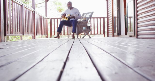 Happy senior african american man spending time in log cabin, playing guitar on balcony - Download Free Stock Photos Pikwizard.com