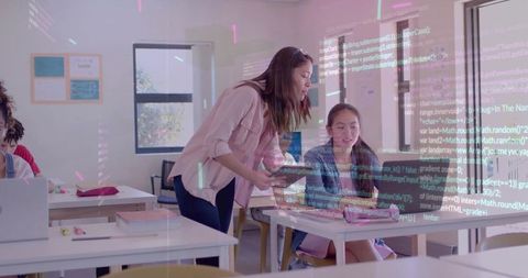 Teacher guiding student coding on laptop with tablet in bright classroom for STEM learning