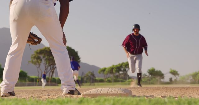 Image captures intense moment in baseball game with player running towards base. Perfect for use in articles or websites related to baseball, sports events, athletic training, or outdoor activities. The dynamic action and clear focus on players can be used to depict teamwork, determination, and competitive sports spirit.