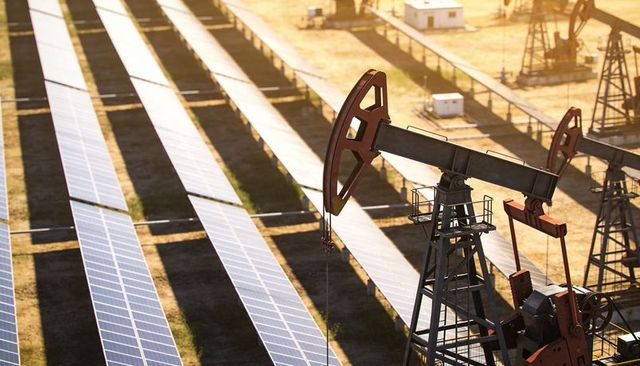 Contrasting energy: operating oil pumpjack beside solar panels at sunrise in arid field