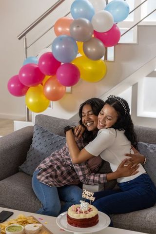 Two young women hugging during 18th birthday celebration with colorful balloons and cake