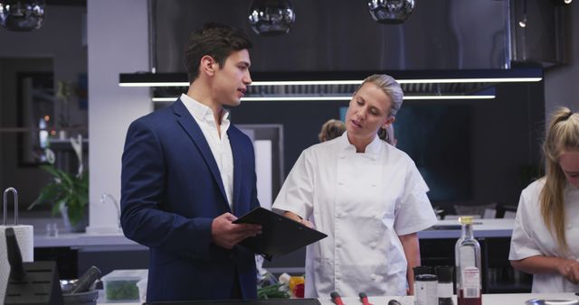 Caucasian female cook in discussion with man in suit using notebook in kitchen. Lifestyle, learning, food, cooking, unaltered.
