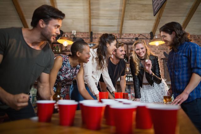 Happy friends playing beer pong game on table in bar