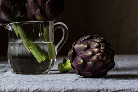 Fresh purple artichokes with water glass on rustic table