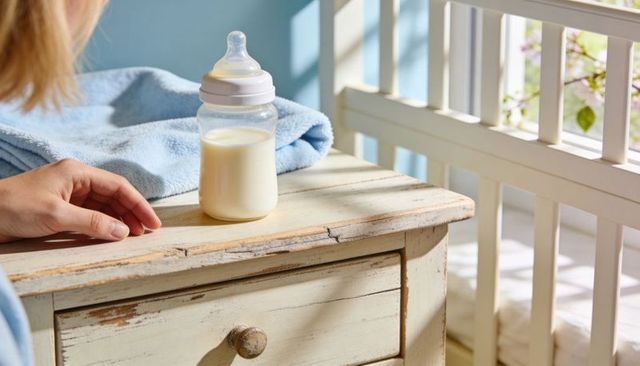 Sunlit nursery baby bottle on rustic nightstand with blue blanket and crib