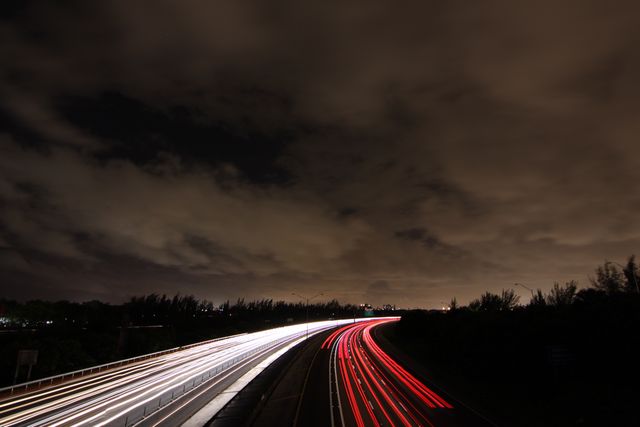 Long exposure capturing light trails of cars speeding on highway during night time under cloudy sky. Ideal for concepts related to urban life, transportation efficiency, late-night commuting, and speed. Useful in advertisements for automotive industries, articles about city infrastructure, or backgrounds for posters and presentations depicting metropolitan lifestyles.