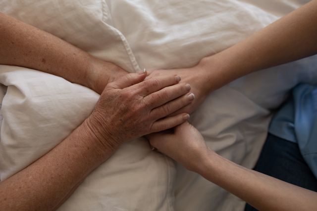 Senior Caucasian woman at home visited by Caucasian female nurse, sitting on bed, holding hands. Medical care at home during Covid 19 Coronavirus quarantine.