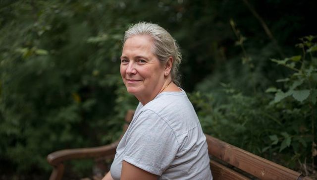 Senior woman sitting on bench turning to camera with gentle smile in green park portrait