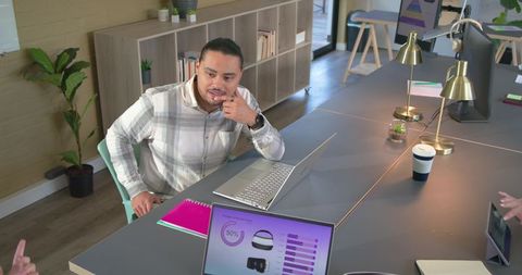Young man leaning on chin thinking during collaborative coworking session at shared desk