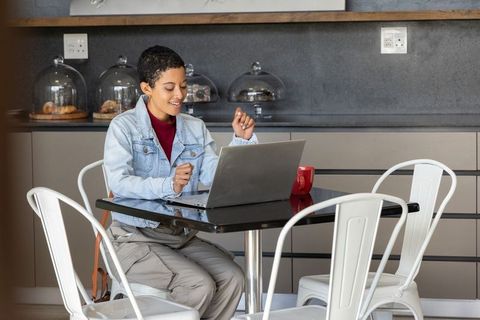 African american woman working remotely in modern cafe with laptop and red mug