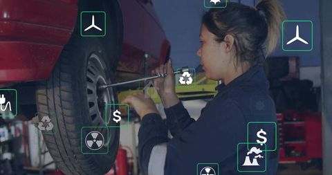Female auto technician tightening wheel lug nuts with breaker bar in garage workshop