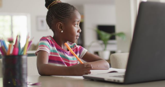 Image of thoughtful african american girl writing during online class on laptop at home, copy space. Education, learning, technology and domestic life.