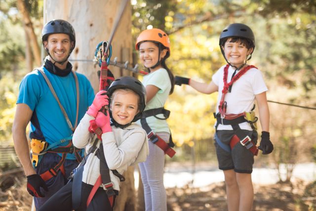 Children having fun on a zip line adventure, wearing safety gear including helmets and harnesses. Great for depicting outdoor activities, team-building events, and family adventures in nature. Ideal for promoting recreational programs, summer camps, and adventure parks.