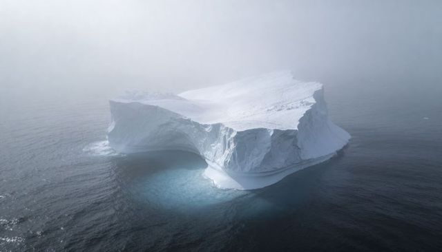Tabular iceberg with undercut arch drifting through misty polar ocean