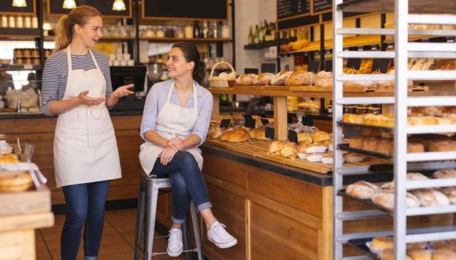 Friendly bakery staff discussing orders at wooden counter surrounded by artisan breads