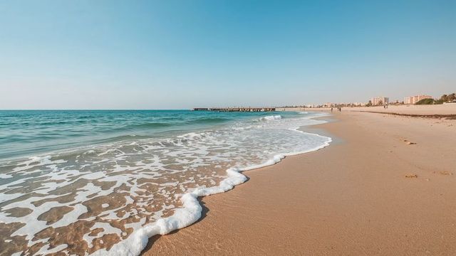 Tranquil Beach with Gentle Waves and Distant Breakwater