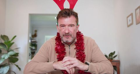 Festive senior man with antlers and garland celebrating at home