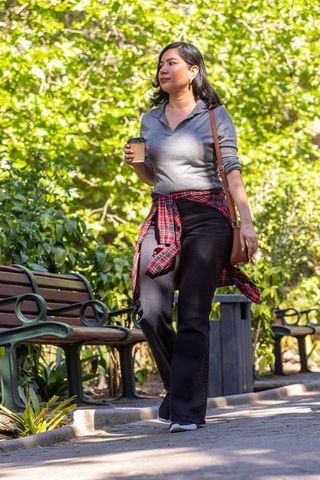 Woman walking in park holding coffee cup with red plaid shirt tied around waist
