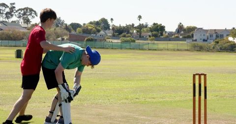 Teen wicketkeeper diving over stumps to stop ball after bat strike on local cricket pitch
