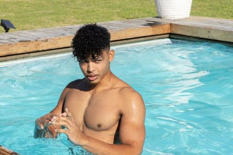 Young african american man cooling off in backyard pool, splashing water in summer sun