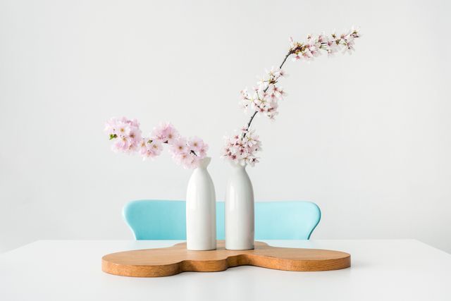 White vases holding delicate sakura blossoms placed on a wooden stand create a minimalist and modern aesthetic. Ideal for illustrating concepts of home decoration, simplicity, and contemporary living. Perfect for websites, blogs, or magazines focusing on interior design, home styling, or modern living.