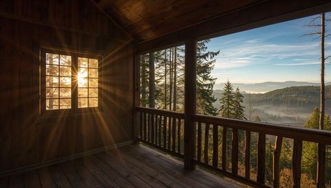 Sunrise framing wooden cabin balcony revealing misty mountain valley through sunlit window
