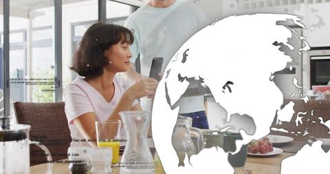 Couple sharing smartphone at breakfast in modern kitchen with digital globe overlay
