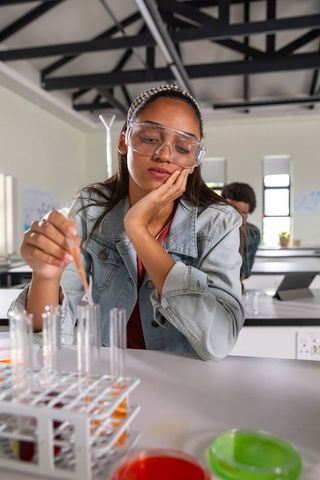 African american teenager pipetting solutions at lab bench wearing safety goggles