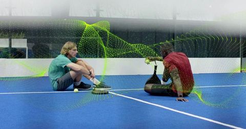Sitting adaptive athletes sharing tennis balls indoor blue court showing prosthetic blade