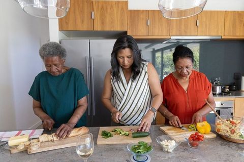 Multigenerational women chopping vegetables and preparing salad together in modern kitchen