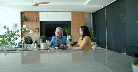 Senior and middle-aged women sharing wine and conversation in modern open-plan kitchen