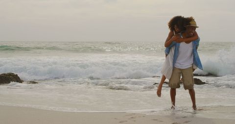 Joyful Couple Piggybacking at Sandy Beach with Waves in Background - Download Free Stock Images Pikwizard.com