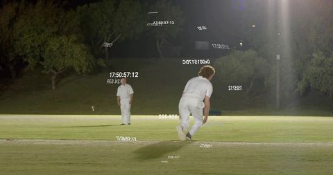 Night cricket bowler sprinting on floodlit pitch in whites with timestamp and code overlays