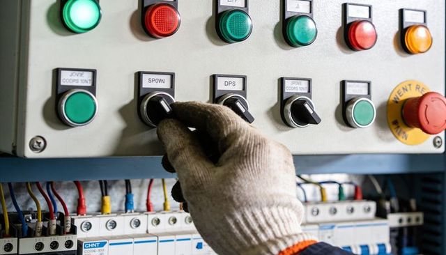 Gloved hand operating DPS rotary selector switch on industrial control panel with wiring