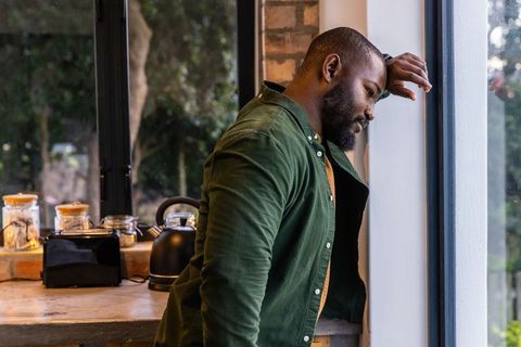 African american man leaning at kitchen window gazing contemplatively, morning light