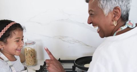Grandmother enjoying cooking session with smiling granddaughter at home