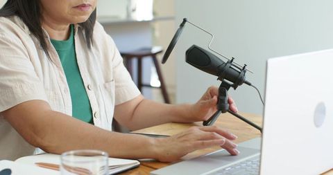 Mature woman recording podcast from home using usb microphone and laptop
