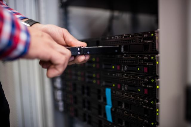 Technician inserting a hard disk drive into a blade server in a data center. Ideal for illustrating concepts related to IT maintenance, data storage, server management, and technology infrastructure. Suitable for use in articles, blogs, and presentations about data centers, IT professionals, and network management.