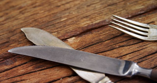 A knife and fork are placed on a rustic wooden table, suggesting a meal setting or preparation for dining. The worn utensils and textured wood surface evoke a cozy, homely atmosphere.