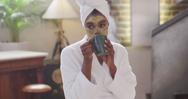 Eafrican american attractive woman with applied face mask drinking coffee and using laptop at home. beauty, pampering, home spa and wellbeing concept.