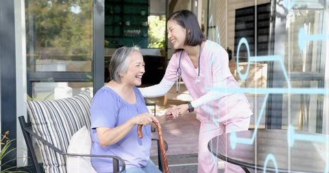 Nurse assisting smiling senior Asian woman on sunny patio, caregiver holding hand